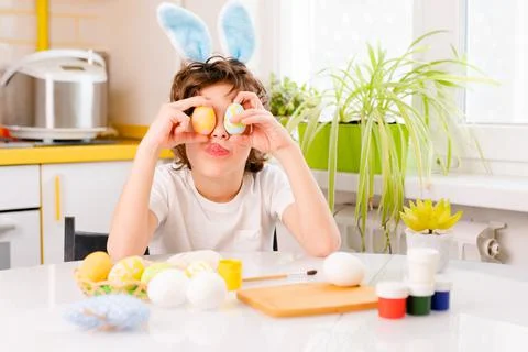 Dyeing Easter eggs. curly boy dressed in white Tshirt and blue bunny ears paints Stock Photos