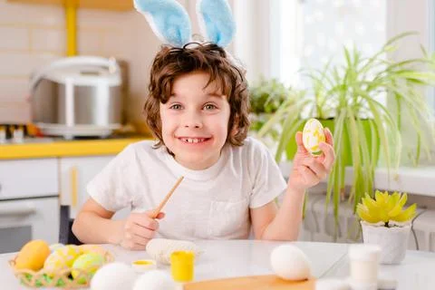 Dyeing Easter eggs. curly boy dressed in white Tshirt and blue bunny ears paints Stock-Fotos