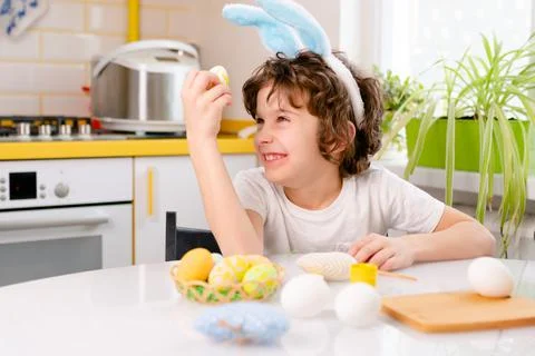 Dyeing Easter eggs. curly boy dressed in white Tshirt and blue bunny ears paints Stock Photos