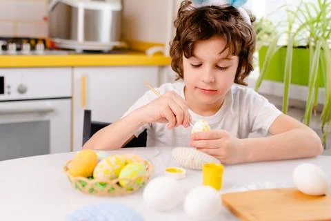 Dyeing Easter eggs. curly boy dressed in white Tshirt and blue bunny ears paints Stock Photos