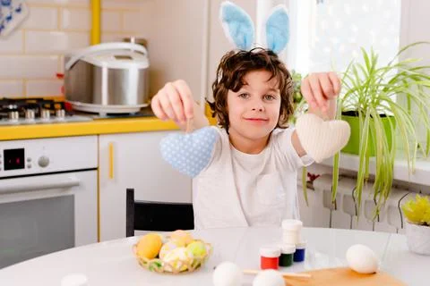 Dyeing Easter eggs. curly boy dressed in white Tshirt and blue bunny ears paints Stock Photos