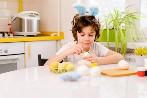 Dyeing Easter eggs. curly boy dressed in white Tshirt and blue bunny ears paints Stock Photos