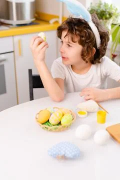 Dyeing Easter eggs. curly boy dressed in white Tshirt and blue bunny ears paints Stock Photos