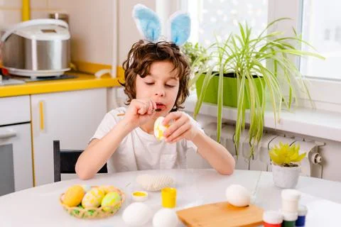 Dyeing Easter eggs. curly boy dressed in white Tshirt and blue bunny ears paints Foto stock