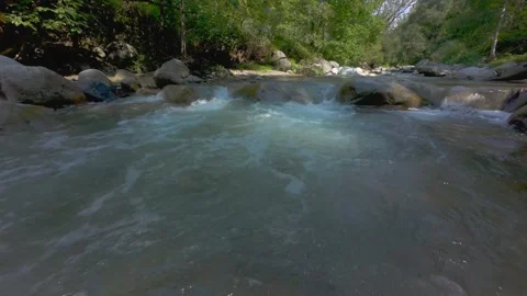 A dynamic aerial flight tracking over a rocky river stream surrounded by green Stock Footage 346222840