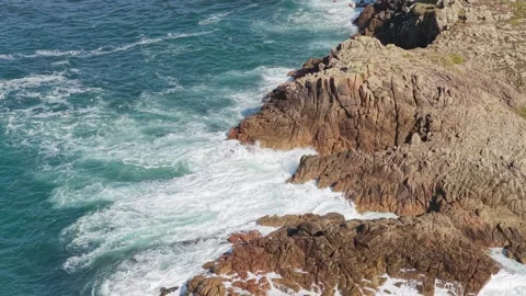 Dynamic aerial footage of ocean waves crashing against rugged rocky cliffs at Stock Footage 346678663