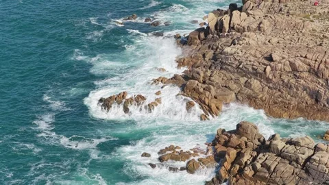 Dynamic aerial footage of ocean waves crashing against rugged rocky cliffs at Stock Footage 346699138
