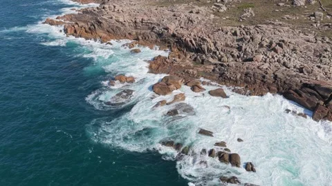 Dynamic aerial footage of ocean waves crashing against a rugged rocky coastline Stock Footage 346699535