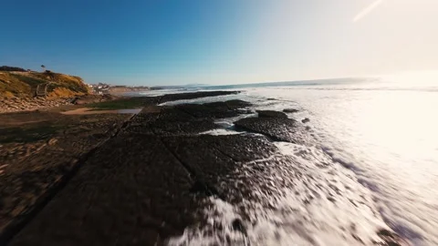 Dynamic aerial shot of waves breaking over rocks under bright sun Stock Footage 339786635