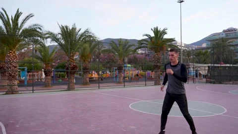 Dynamic Boxing Practice: Guy's Shadowboxing Session on Palm-Lined Basketball Stock Footage 243169394