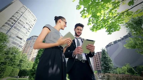 Dynamic business duo joyfully collaborating on tablets in an urban setting Video stock 311645934