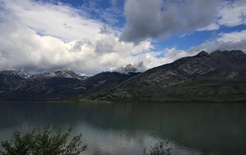 Dynamic clouds sweeping over rugged mountain peaks and a calm lake Stock Photos