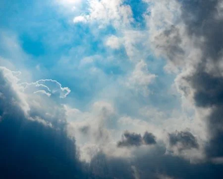 Dynamic Cloudscape: Sunlit Blue Sky &amp; Dramatic Grey Clouds 写真素材