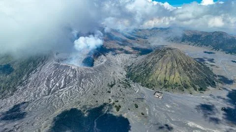 Dynamic duo of Bromo steaming crater and Batok cone amid ash plains and swirling Foto stock