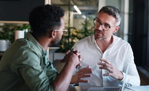 A dynamic duo that gets things done. two businessmen using a laptop and having a Stock Photos