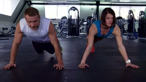 Dynamic duo performing synchronized push-ups in a modern gym Stock Footage 311545362