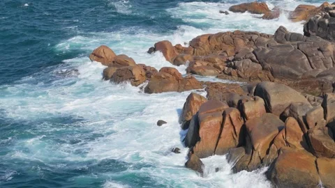 Dynamic footage of ocean waves crashing against rugged, reddish-brown granite Stock Footage 346692385