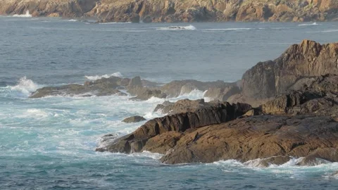 Dynamic footage of ocean waves crashing against rugged dark rocks along the Stock Footage 346709689