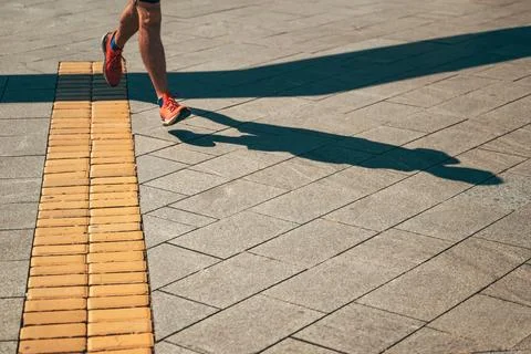 Dynamic high angle view of a runner's legs and shadow on urban pavement in .. Stock Photos