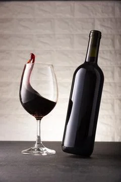 Dynamic image of unlabeled red wine bottle and wine glass with wine flowing i Stock Photos