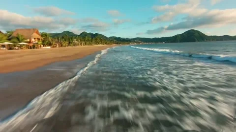 Dynamic Low Angle Beach Wave Washing Shore with Tropical Resort Stock Footage 319928189