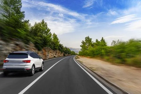 A dynamic low-angle shot captures a modern white SUV driving quickly along a Stock Photos