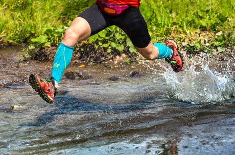 Dynamic man running in the mountain, jumping over a creek Stock Photos