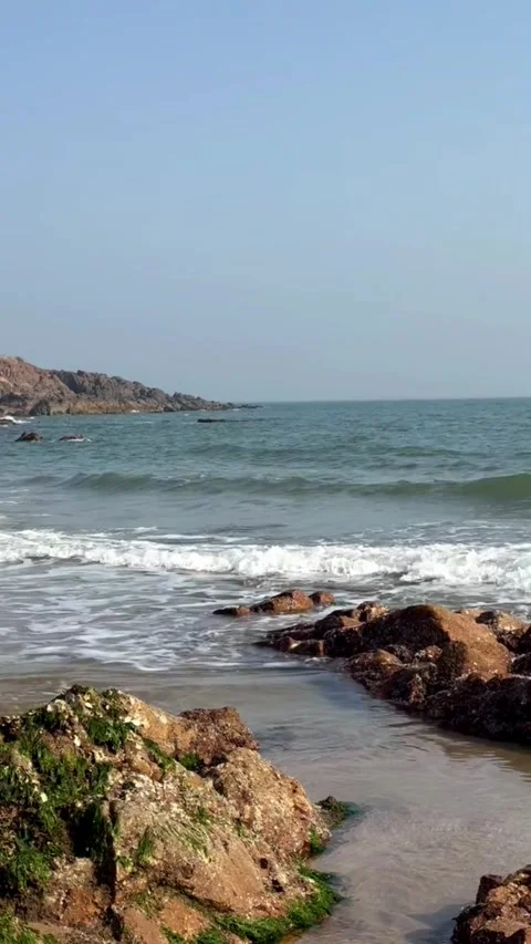 Dynamic ocean waves crash onto a rugged, rocky coastline under a clear blue sky, Stockbeeldmateriaal 333605297