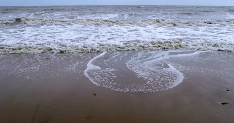 Dynamic Ocean Waves Flowing Across a Sandy Shoreline Under Overcast Skies in 스톡 동영상 347403054