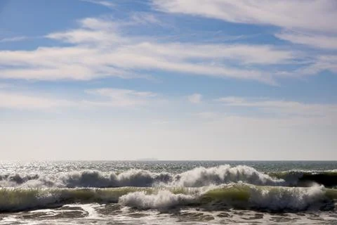 Dynamic ocean waves under a bright blue sky with soft clouds Photos