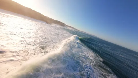 Dynamic perspective shows sea surging with force, sun rising over cliffs 库存影片 346371461
