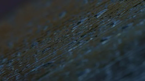 Dynamic rain droplets fall gracefully, creating ripples on a dark and textured Stock Footage 309335776