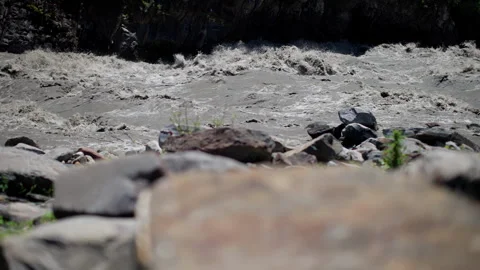 Dynamic river rapids seen over smooth boulders under sunny sky, invoking the Stock Footage 265483600