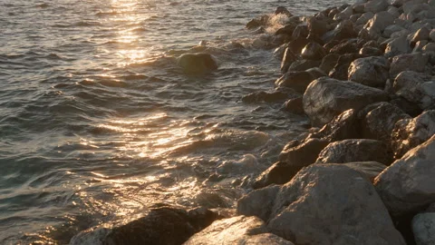 Dynamic sea waves splash against wet rocks on the shore at golden hour Stock Footage 318385484