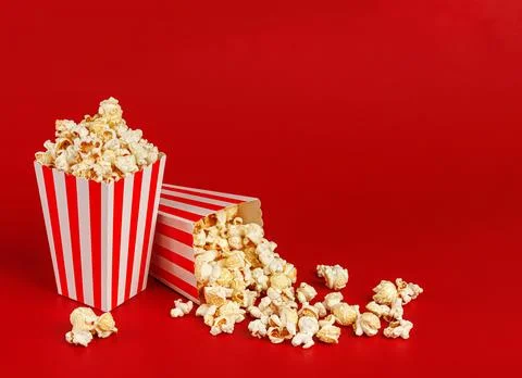 Dynamic shot of a popcorn box tipped over with kernels spilling out on a vibr Stock Photos