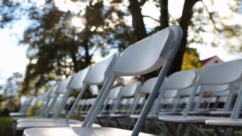 Dynamic shot of white folding chairs outside with sun shining through 스톡 동영상 96544576