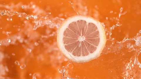 Dynamic slow motion water streams splash citrus fruit slice on orange beverag Stock Footage 327573025