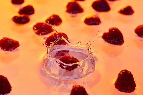 Dynamic splash of raspberry hitting water, with scattered berries in background Stock Photos