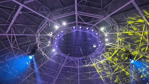 Dynamic Stage Lights Illuminate the Geometric Steel Ceiling of a Large Arena Stock Footage 329455751
