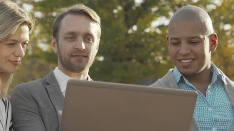 Dynamic teamwork in a park: three colleagues collaborating on a laptop Stock Footage 311526221