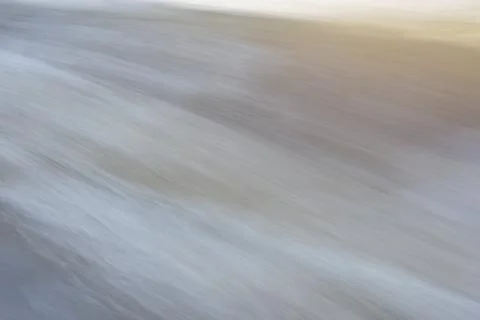 Dynamic texture of fast moving water, in pastel pale neutral tones. Stock Photos