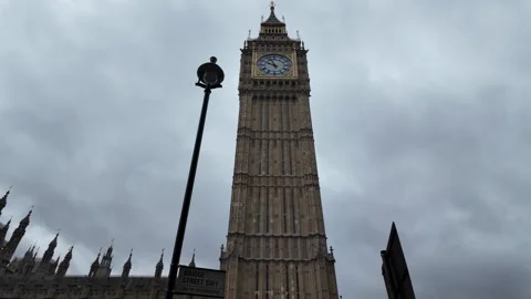 Dynamic upward pan of Elizabeth Tower clock face under overcast London sky Stock Footage 346677879