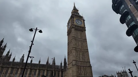 Dynamic upward pan of Elizabeth Tower and Palace of Westminster on cloudy day Stock Footage 346677963