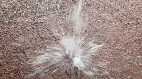 A dynamic water splash captured on a brick pavement, showing droplets in mid-air Video stock 306253861