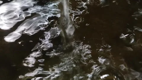 Dynamic Water Stream Creating Abstract White Foam and Ripples on a Dark Surface Stock Footage 334327729