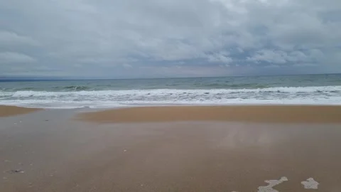 Dynamic waves crashing onto beach shoreline under dramatic cloudy sky Stock Footage 322040765