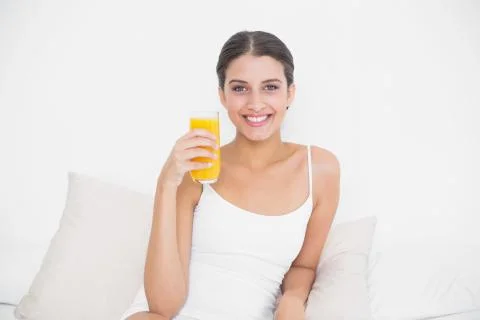Dynamic young brown haired model in white pajamas holding a glass of orange Stock Photos