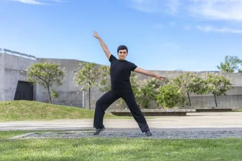 Dynamic young man striking a pose with outstretched arms in a park Stock Photos