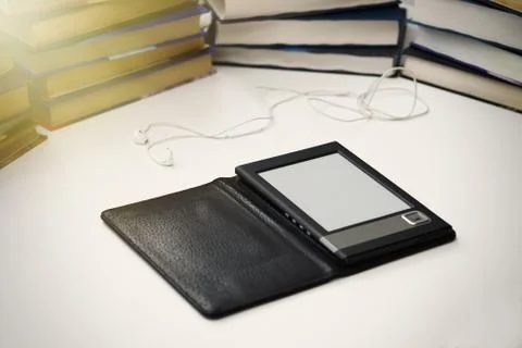 E-book lies on a white table on a background of paper books. Stock Photos