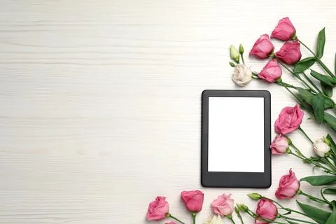 E-book reader with flowers on white wooden table, flat lay. Space for text Stock Photos